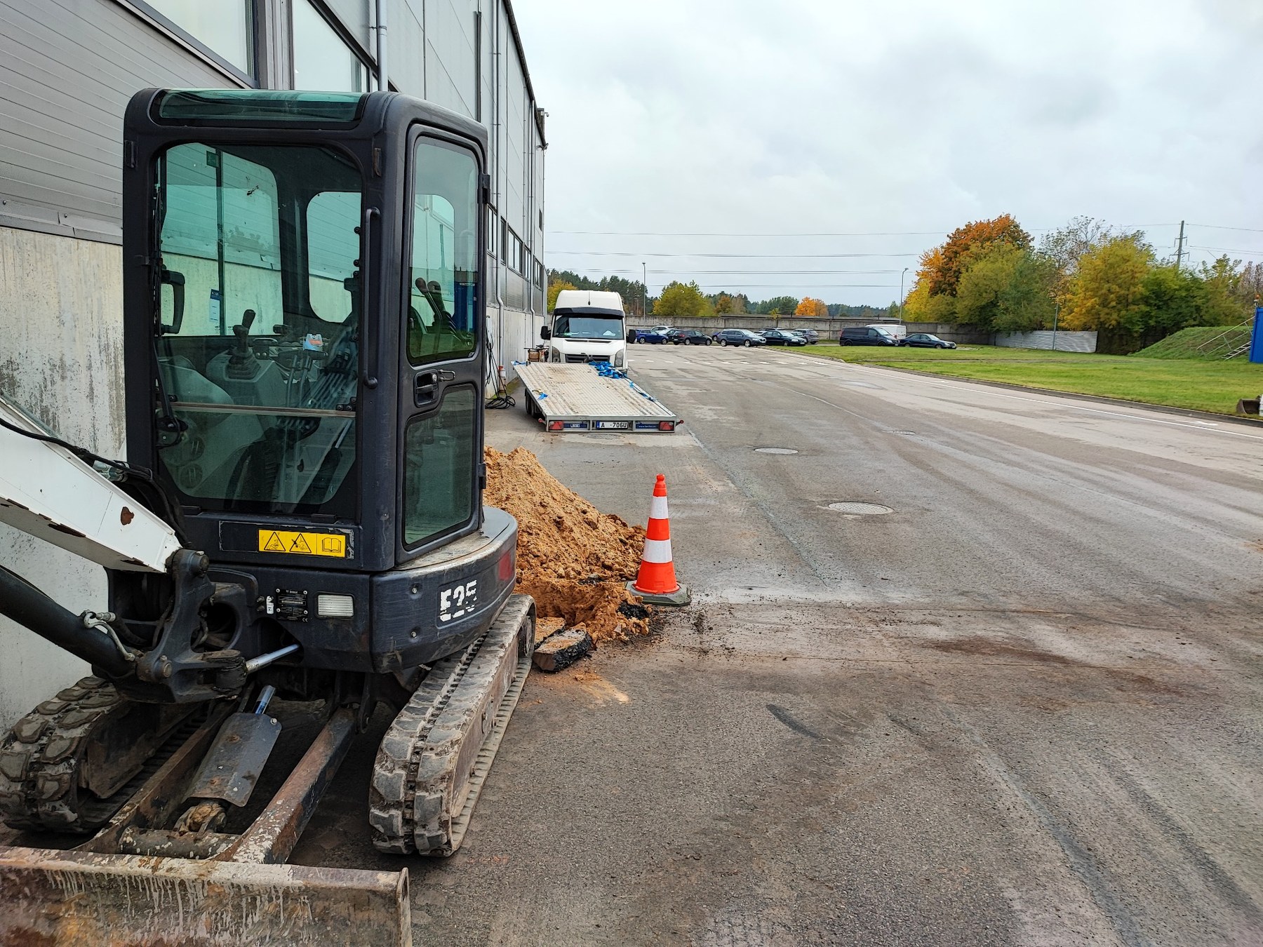 Mini ekskavators darba zonā pie industriālas ēkas
